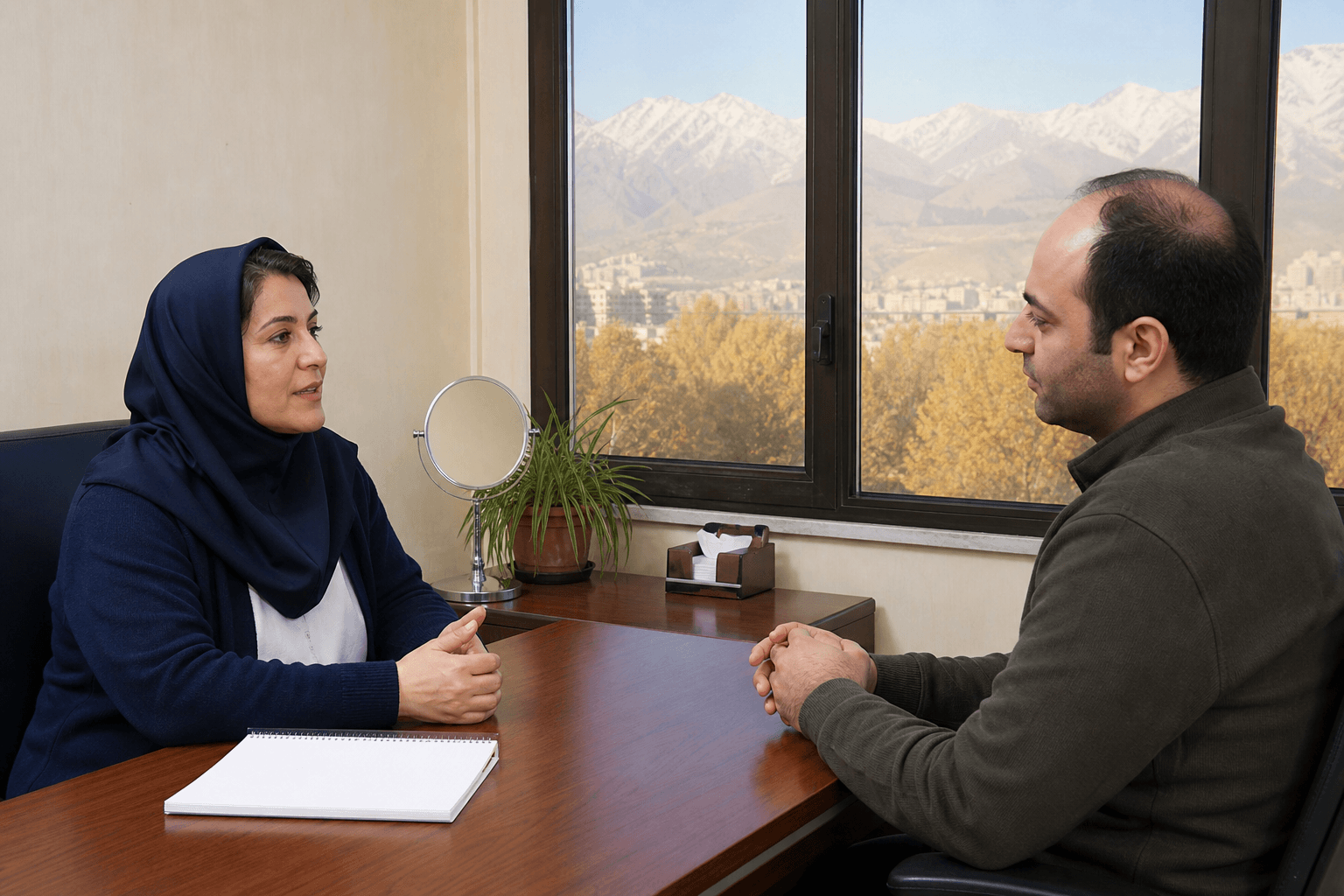 زن پزشک و مرد با ریزش مو پشت میز چوبی کلینیک در تهران، کوه از پنجره دیده می‌شود